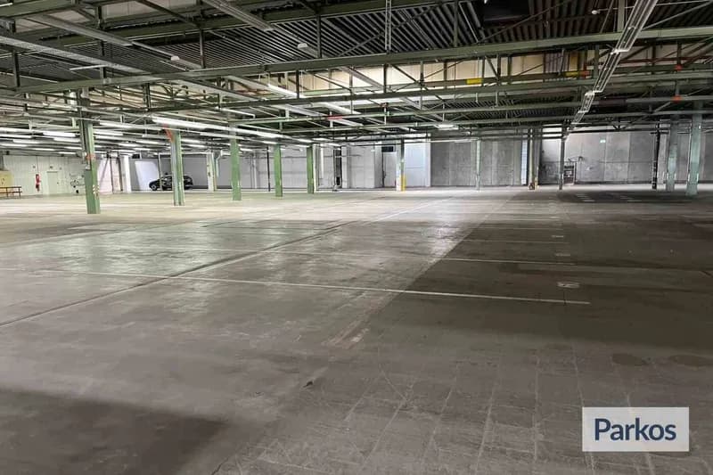 Leere Parkhalle mit Betonboden, grünen Stützsäulen, Deckeninstallationen und einem Auto am linken Rand.