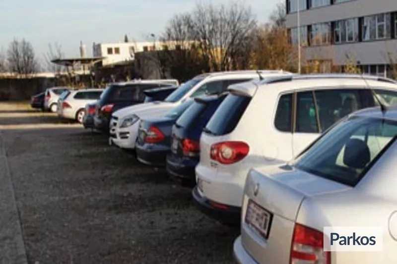 Reihe geparkter Autos auf einem Freiluftparkplatz neben einem mehrstöckigen Gebäude und Bäumen.