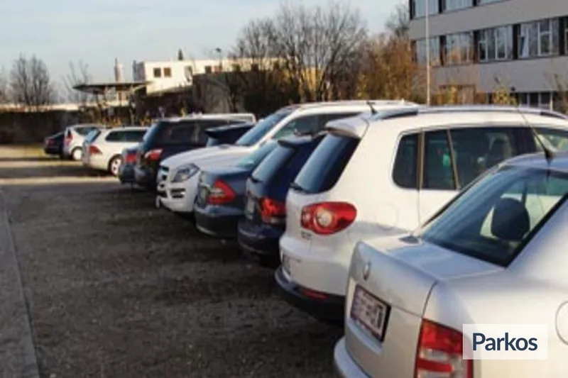 Mehrere nebeneinander geparkte Autos auf einem offenen Parkplatz mit Gebäuden im Hintergrund.