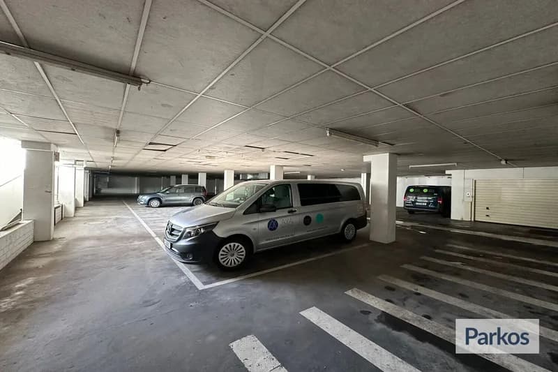Überdachte Parkgarage mit AYA Transferbus auf einem Parkplatz, Säulen und markierte Fahrstreifen.