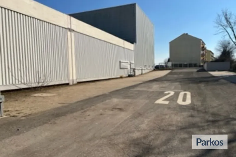 Freifläche mit aufgemalter Zahl 20 auf Asphalt, lange weiße Wellblechhalle links und Gebäude im Hintergrund unter blauem Himmel.