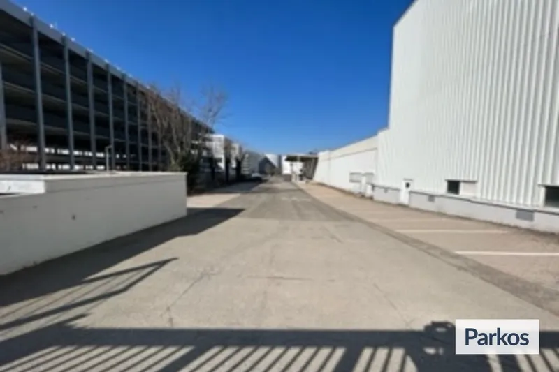 Blick über eine Einfahrt mit Schatten eines Metalltores, links Parkhaus, rechts weiße Halle am Flughafen Stuttgart.