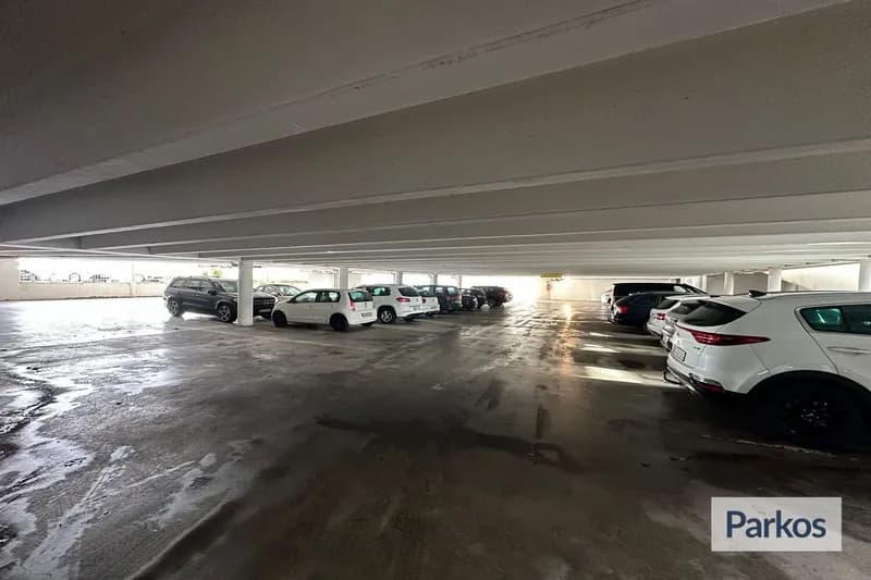 Überdachtes Parkdeck mit Reihen geparkter Autos, Betonstützen und nassem Boden.