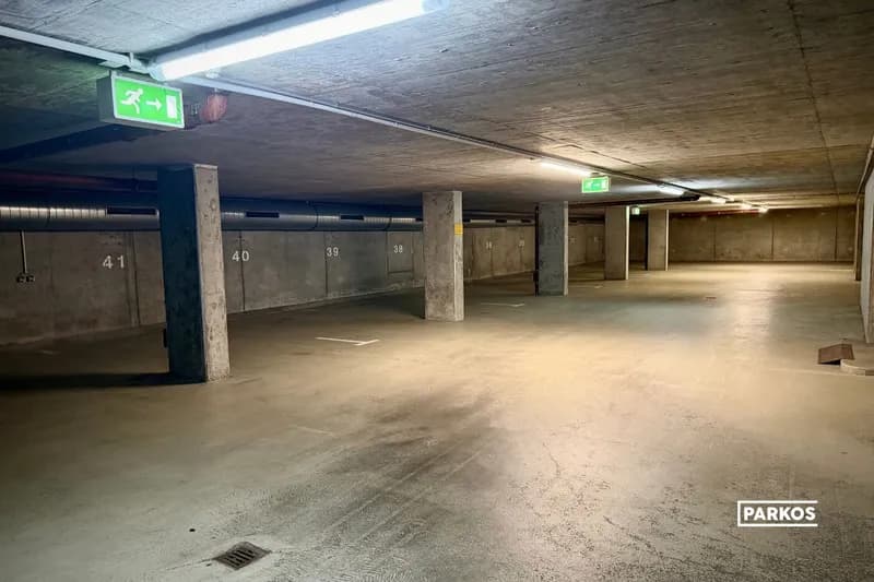 Überdachter Tiefgaragenbereich mit nummerierten Stellplätzen, Betonsäulen und grünen Notausgangsschildern.