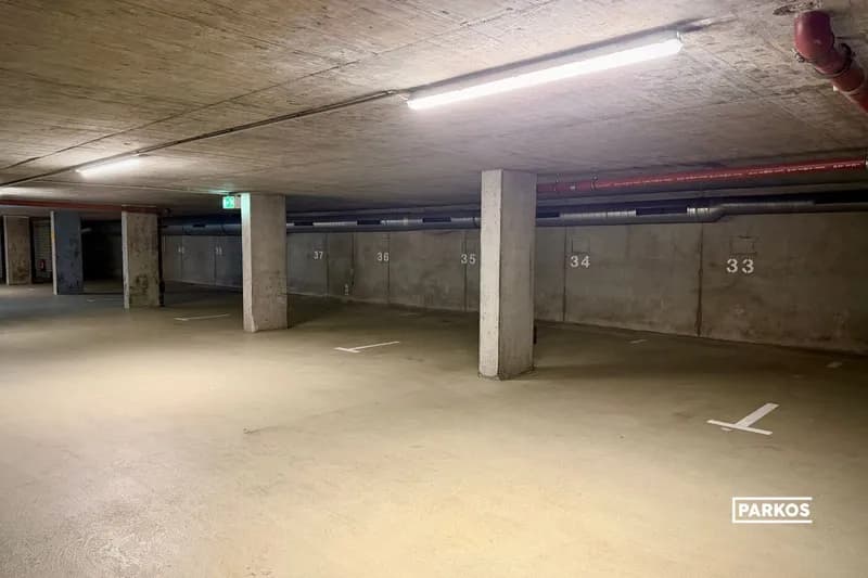 Leere Tiefgarage mit Betonstützen, Deckenleuchten und markierten Stellplätzen nummeriert 33 bis 37.