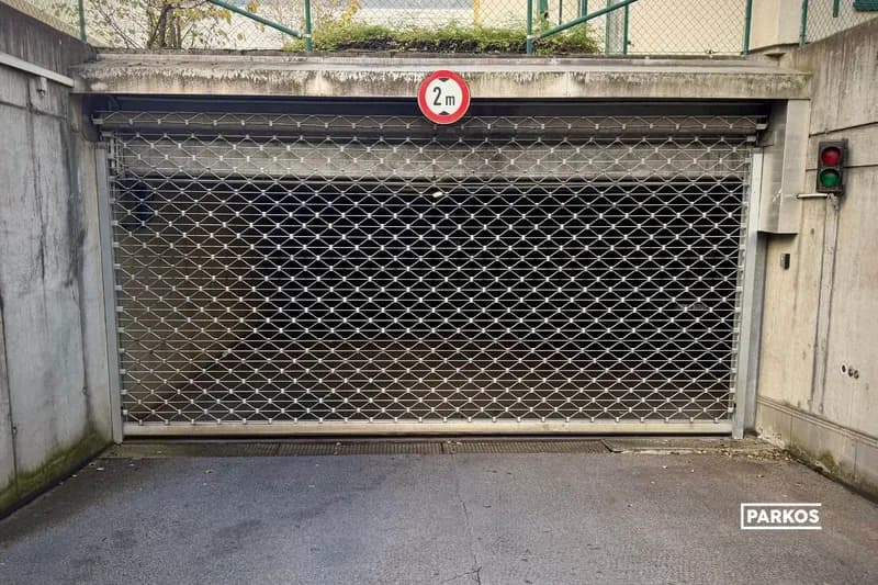 Metallgitter vor der Einfahrt zu einer Tiefgarage, 2-m-Höhenbegrenzungsschild oberhalb und Ampel an der Betonwand.