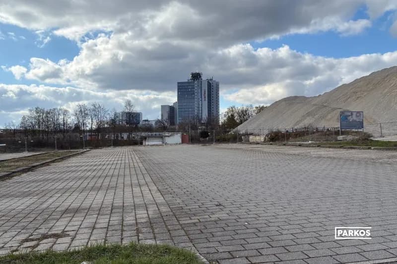 Gepflasterte Parkfläche mit leerer Stellfläche, aufgeschüttetem Hügel rechts und Hochhaus im Hintergrund am Flughafen Stuttgart.