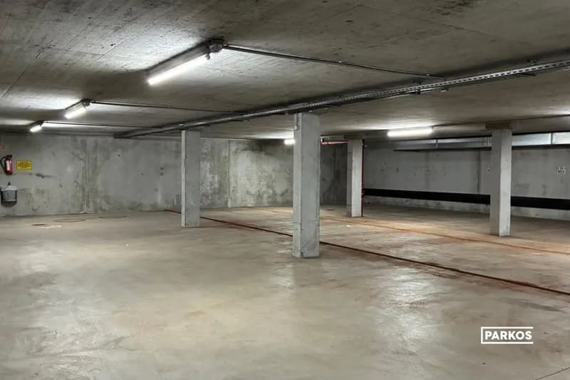 Überdachte Tiefgarage mit Betonstützen, Deckenleuchten und einem Feuerlöscher an der Wand.