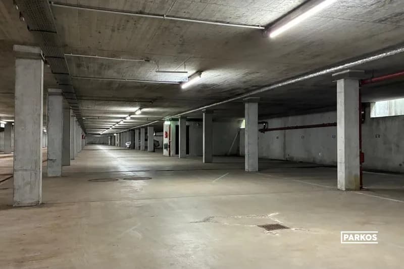 Tiefgarage mit Betonstützen, Deckenleuchten, markierten Parkplätzen und Bodenablauf.