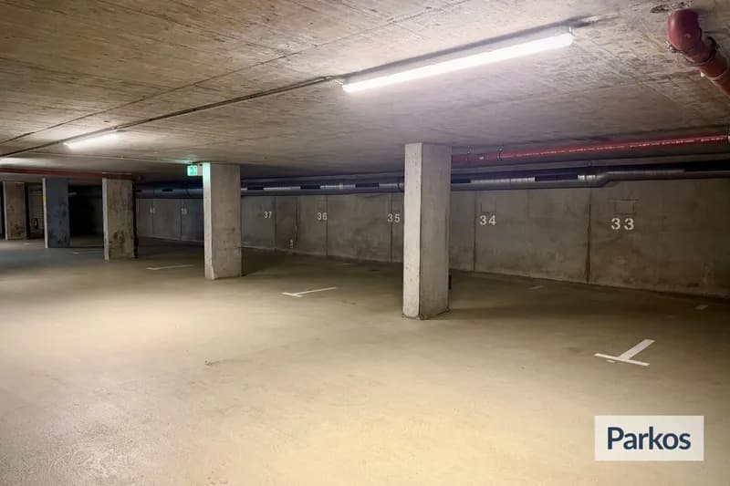Überdachte Parkebene mit nummerierten Stellplätzen 33 bis 37, Betonpfeilern und Notausgangszeichen.