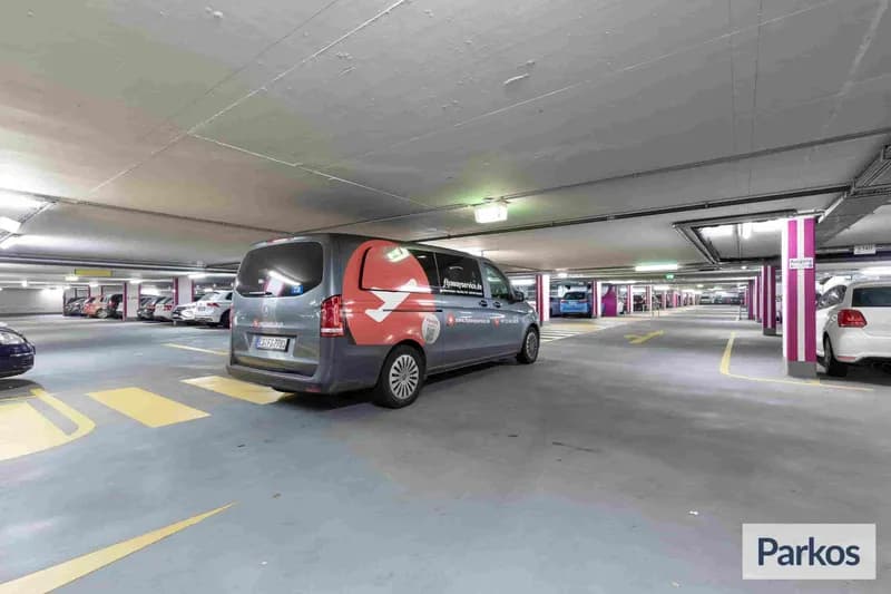Überdachte Tiefgarage mit FlyAway Service Shuttlebus neben markierten Fahrwegen und geparkten Autos.