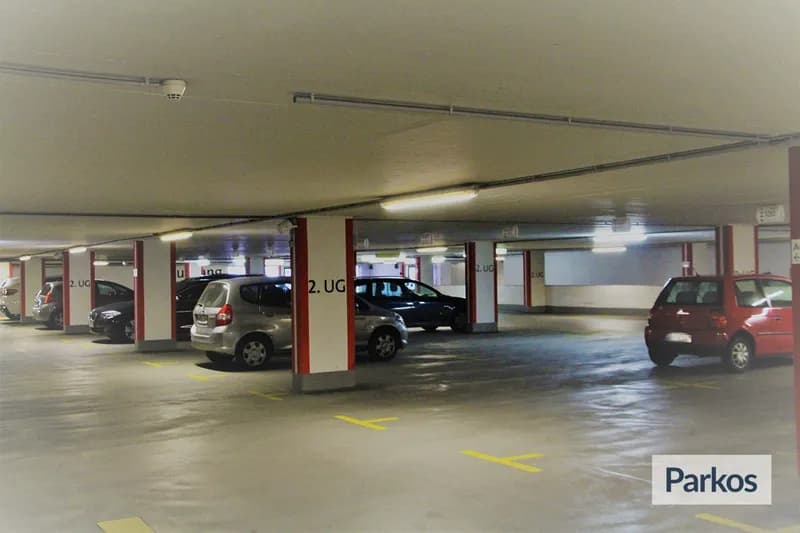 Tiefgarage mit mehreren geparkten Autos, Säulen mit Beschriftung 2. UG und Überwachungskamera an der Decke.