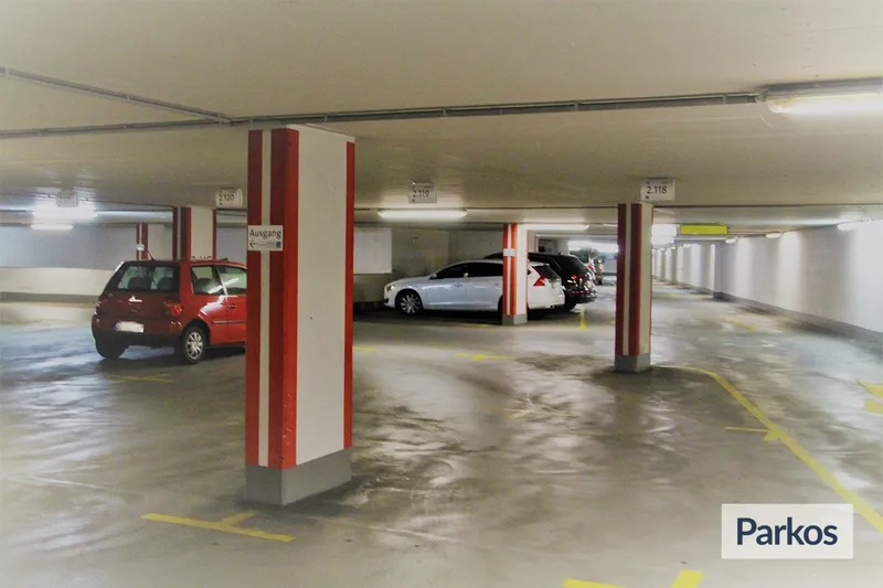 Überdachte Parkgarage mit rot gestreiften Säulen, mehreren geparkten Pkw und Bodenmarkierungen.