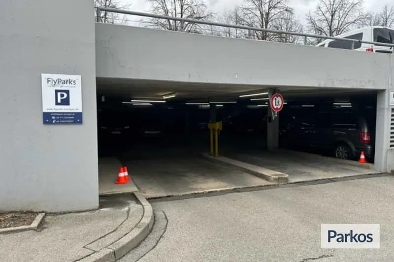 Überdachte Parkhauseinfahrt mit FlyParks-Schild, orangen Absperrkegeln und geparktem Auto im Halbdunkel.