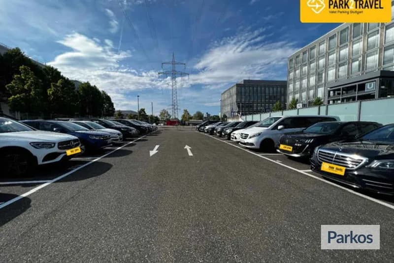 Freiluftparkplatz mit zwei Parkreihen, geparkten Autos, Fahrbahnpfeilen und Strommast im Hintergrund.