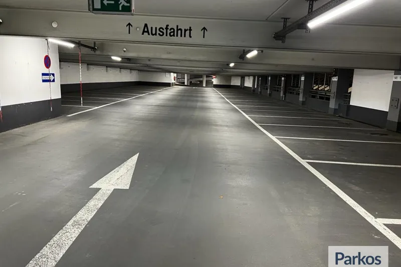 Leeres überdachtes Parkdeck mit markierten Stellplätzen, Fahrbahnpfeil und Ausfahrt-Schild an der Decke.