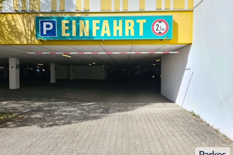 Überdachte Parkhauseinfahrt mit Schild EINFARHT, Parksymbol und Höhenbegrenzung 2,1 m, gepflasterte Zufahrt.