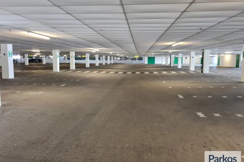 Leeres überdachtes Parkdeck mit Fahrgasse, markierten Stellplätzen, weißen Stützen und Deckenbeleuchtung.