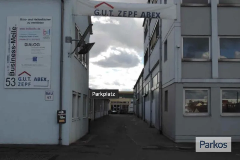 Durchfahrt zwischen zwei Industriegebäuden mit Schild G.U.T. ZEPF ABEX und Parkplatzhinweis, wolkiger Himmel.
