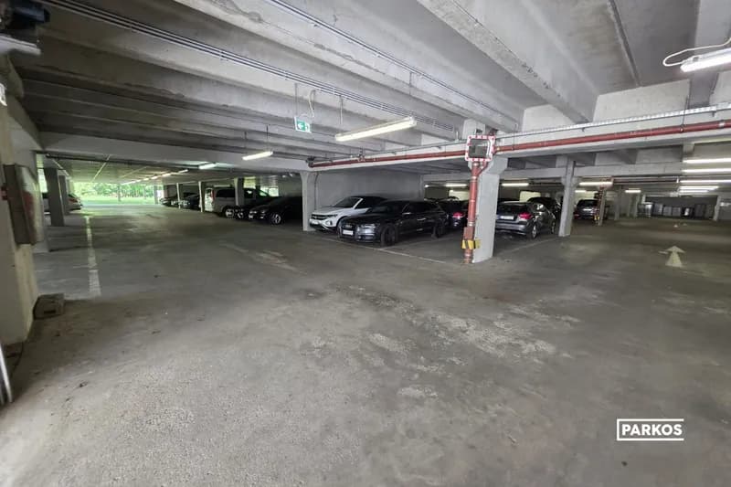Überdachter Parkbereich mit geparkten Pkw, Betonstützen, Deckenbeleuchtung und Ausfahrt ins Freie.
