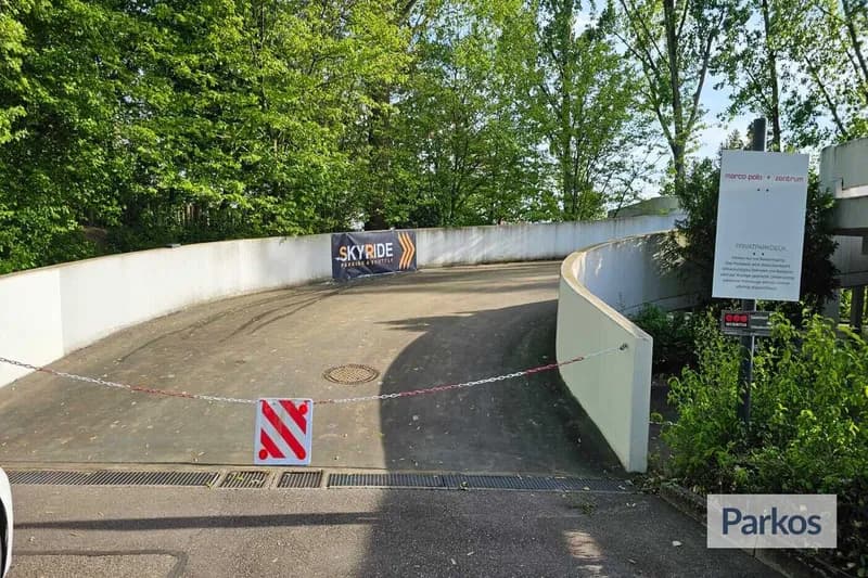 Zufahrt zu geschlossener Parkdeckrampe mit Absperrkette und Skyride-Banner, umgeben von Bäumen.
