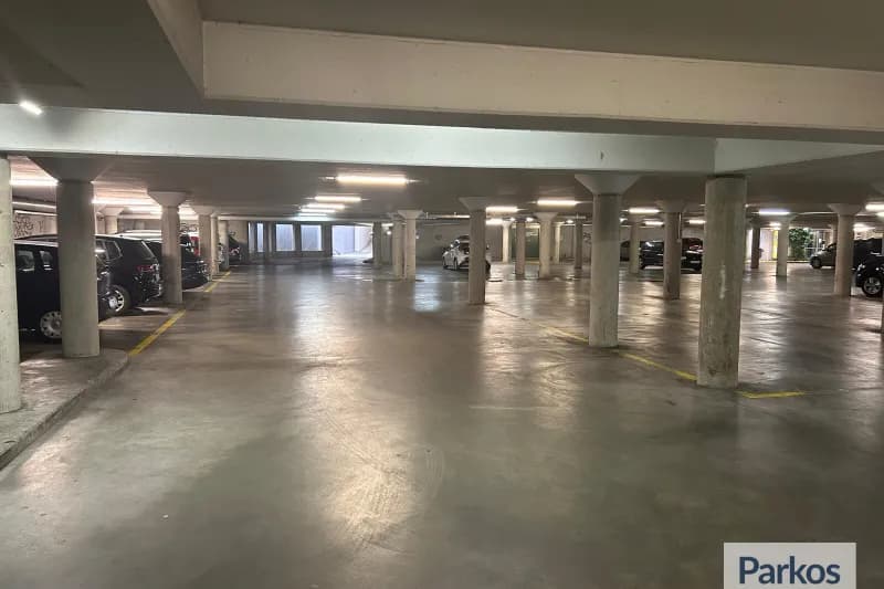 Überdachte Parkgarage mit Betonpfeilern, leeren Fahrspuren und Fahrzeugen an den Seiten.