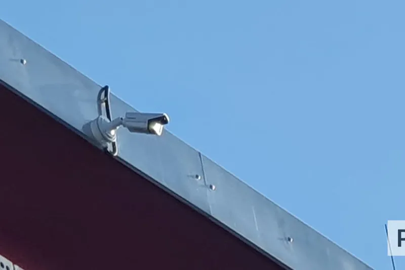 Überwachungskamera an der Dachkante eines Parkplatzgebäudes vor blauem Himmel.