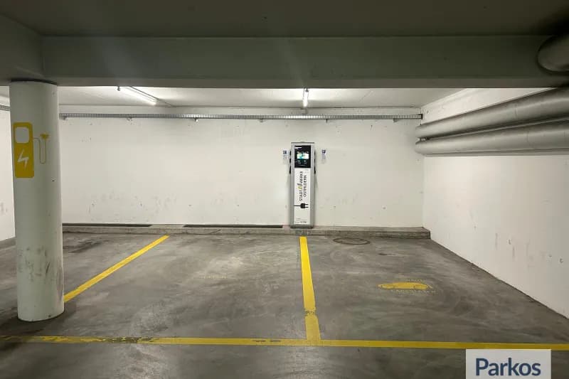 Überdachter Parkbereich mit zwei markierten Stellplätzen, Säule mit Ladekennzeichnung und Wandladegerät.