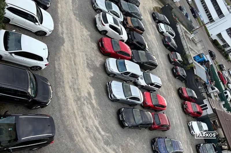 Vogelperspektive auf einen Schotterparkplatz am Flughafen mit mehreren geparkten Autos in Reihen.