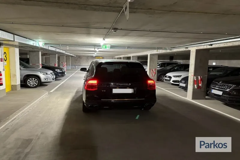 Tiefgarage mit schwarzem Porsche Cayenne S mittig, umgeben von anderen geparkten Autos und Betonstützen.