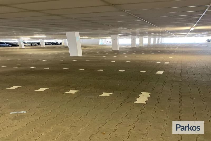 Überdachter Parkplatz mit markierten Stellflächen, Stützsäulen und wenigen Autos am Rand, heller Ausgang im Hintergrund.