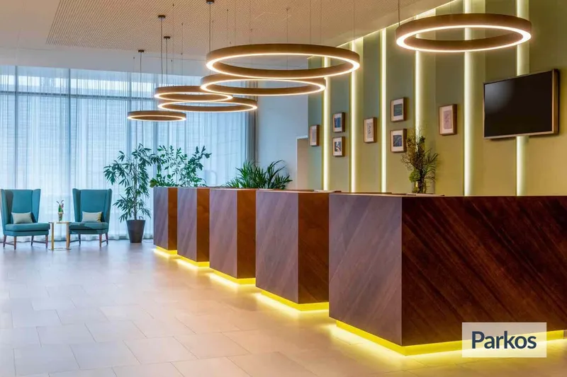 Hotelrezeption mit mehreren hölzernen Empfangstheken, beleuchteten Ringen an der Decke und Sitzbereich am Fenster.