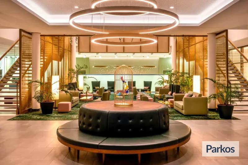 Hotelhalle mit runder gepolsterter Sitzbank, dekorativem Vogelkäfig, Ringleuchtern, Treppen und Sofagruppen.