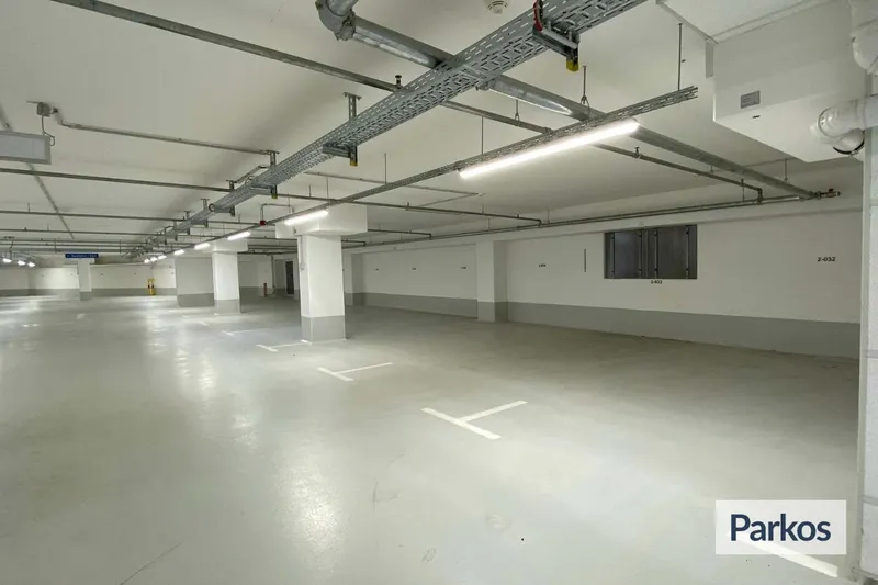 Leeres überdachtes Parkhaus mit Betonstützen, markierten Stellflächen und sichtbaren Deckenleitungen.
