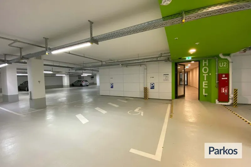 Überdachtes Parkhaus mit markierten Stellplätzen, Behindertenkennzeichnung und grünem Hotelzugang mit Schrift HOTEL.