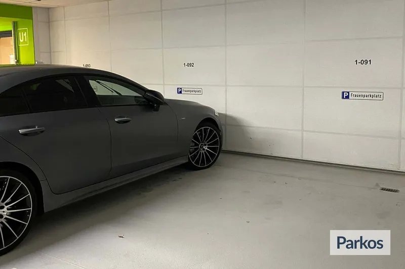 Dunkles Auto steht in überdachtem Parkhaus an markierten Frauenparkplätzen neben Wand mit Stellplatznummern.